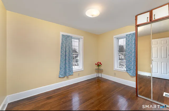 an empty room with wooden floor and windows with curtains
