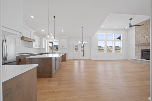 1117 East Shilow Road, Unit 106 Erda, UT 84074 - Photo 5 of 21 Open-concept living space featuring a gourmet kitchen with stainless steel appliances, a large central island with seating, wood-finish flooring, a stone-clad fireplace with a wood mantle, and expansive windows