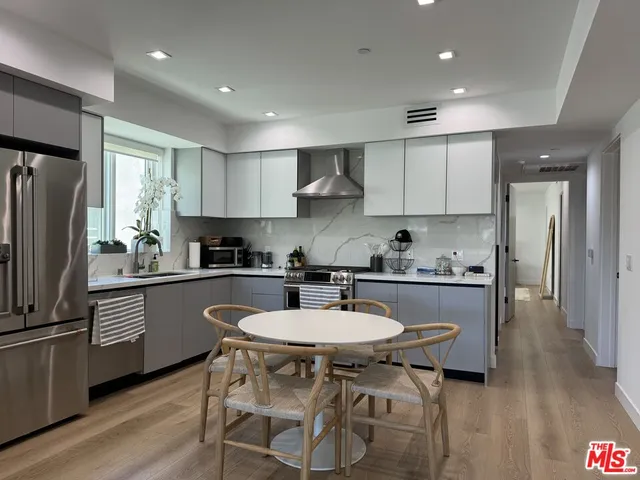 a kitchen with stainless steel appliances granite countertop a sink a stove a refrigerator and white cabinets with wooden floor