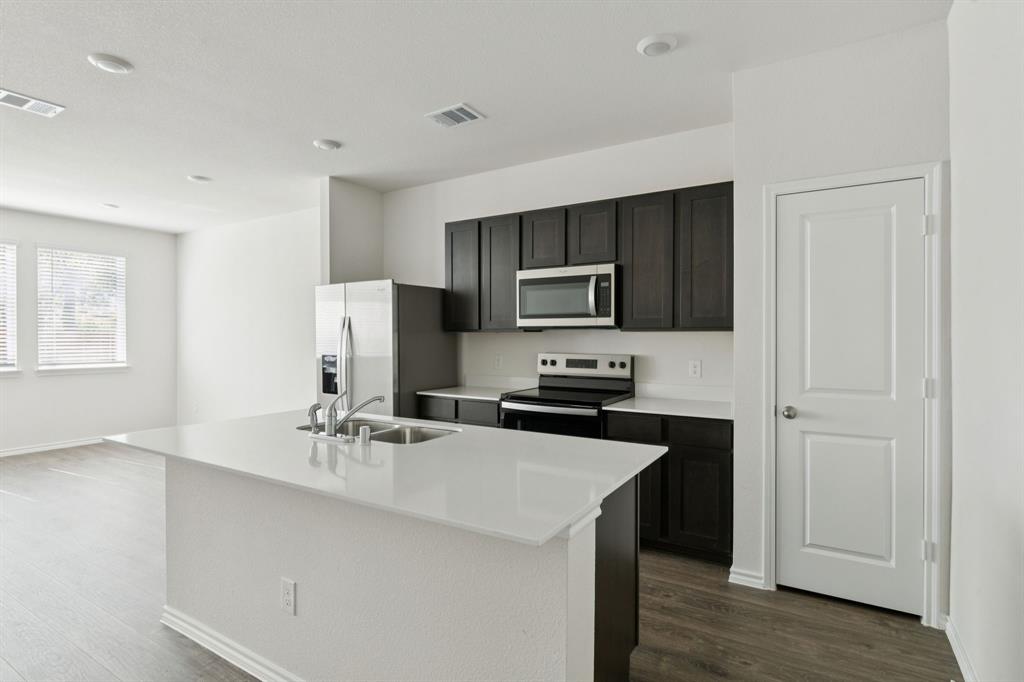 317 Clematis Street Princeton, TX 75407 - Photo 11 of 38 Kitchen with appliances with stainless steel finishes, dark wood-type flooring, a center island with sink, light stone countertops, and dark cabinetry