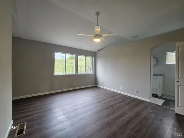 an empty room with wooden floor a ceiling fan and windows
