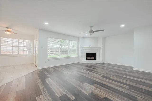 an empty room with wooden floor fireplace and windows