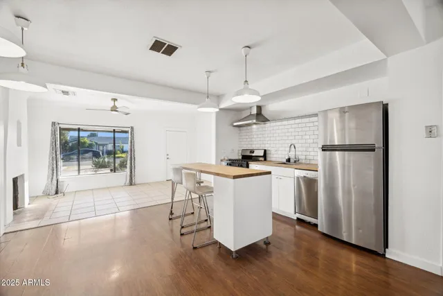 a kitchen with stainless steel appliances kitchen island a refrigerator a sink dishwasher a stove and white cabinets with wooden floor