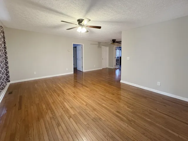 an empty room with wooden floor chandelier fan and windows