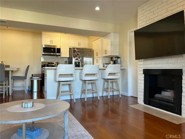 a living room with stainless steel appliances a fireplace a flat screen tv and kitchen view