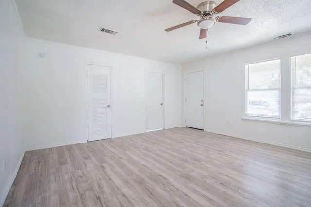 an empty room with wooden floor fan and windows