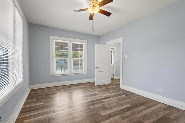 an empty room with wooden floor chandelier fan and windows