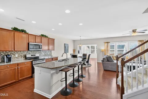 a kitchen with stainless steel appliances granite countertop a stove top oven a sink dishwasher a dining table and chairs with wooden floor