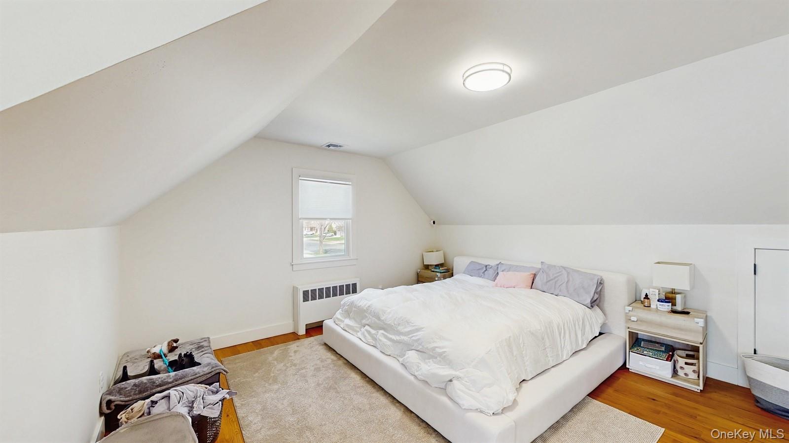 170 Wetherill Road Garden City, NY 11530 - Photo 17 of 23 Bedroom with visible vents, radiator heating unit, vaulted ceiling, and wood finished floors