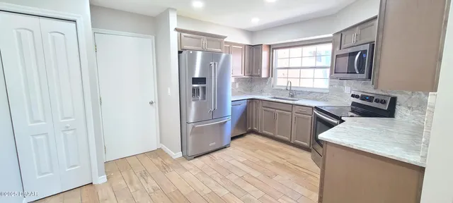 a kitchen with stainless steel appliances granite countertop a refrigerator a sink dishwasher a stove with wooden cabinets and floors