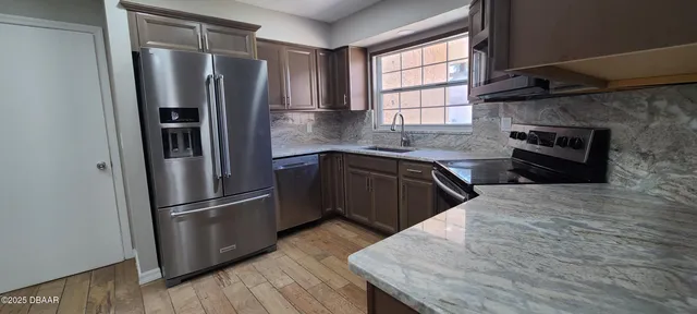 a kitchen with stainless steel appliances granite countertop a refrigerator a sink dishwasher a stove and white countertops with wooden floor