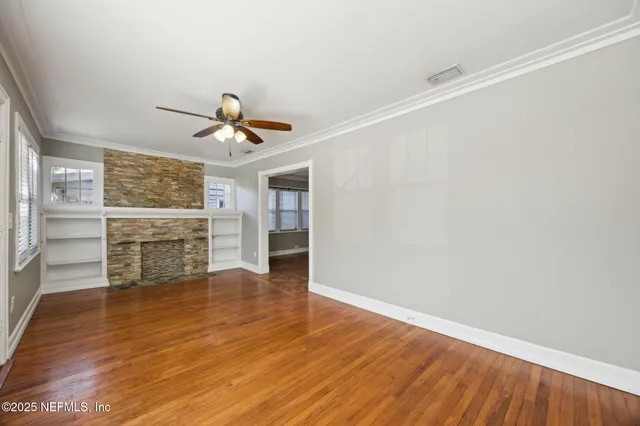 a view of a livingroom with wooden floor a ceiling fan and windows
