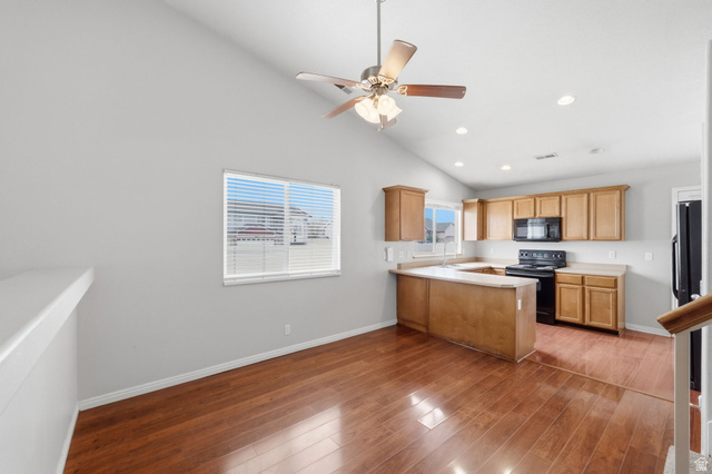 2575 Athena Drive Magna, UT 84044 - Photo 5 of 23 Open-concept living space featuring wood-finish flooring, a vaulted ceiling with a ceiling fan, and a kitchen with warm-toned cabinetry, a black electric range, and a black built-in microwave