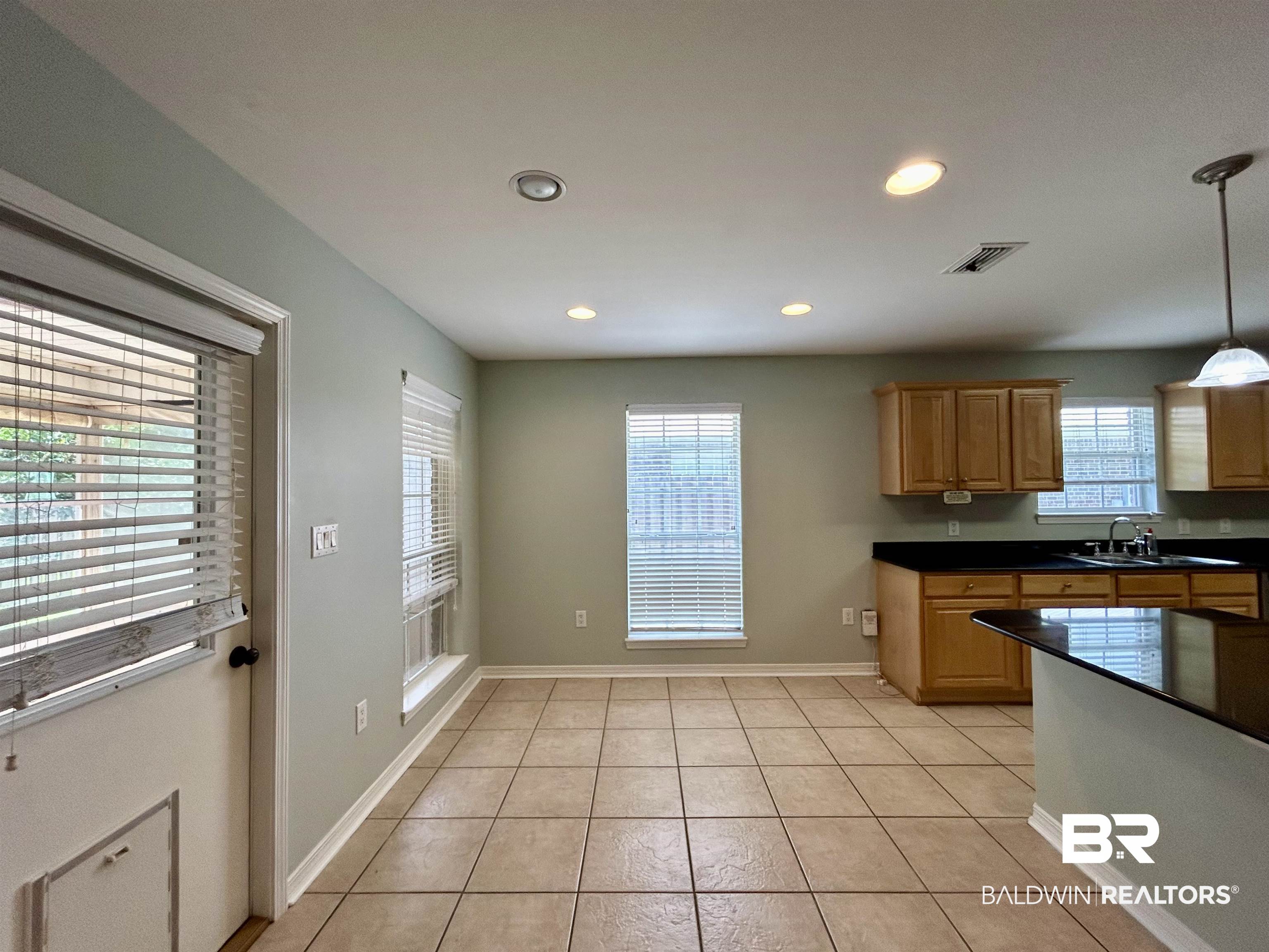 7198 Raintree Lane Gulf Shores, AL 36542 - Photo 5 of 33 Spacious kitchen and dining area featuring tile flooring, recessed lighting, wood cabinetry, dark countertops, and multiple windows with blinds