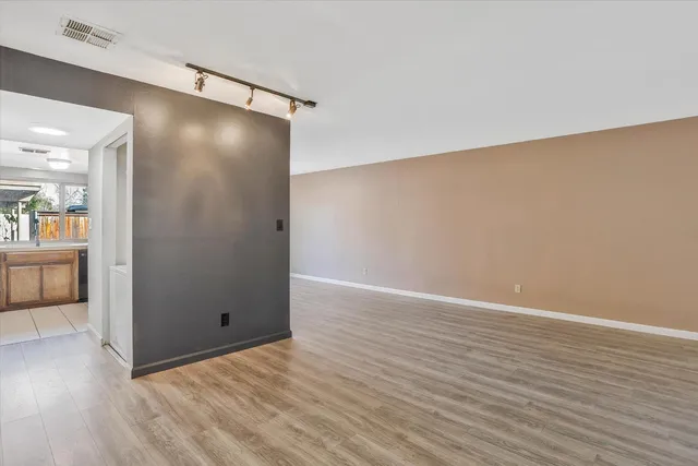 a view of an empty room with wooden floor and a kitchen