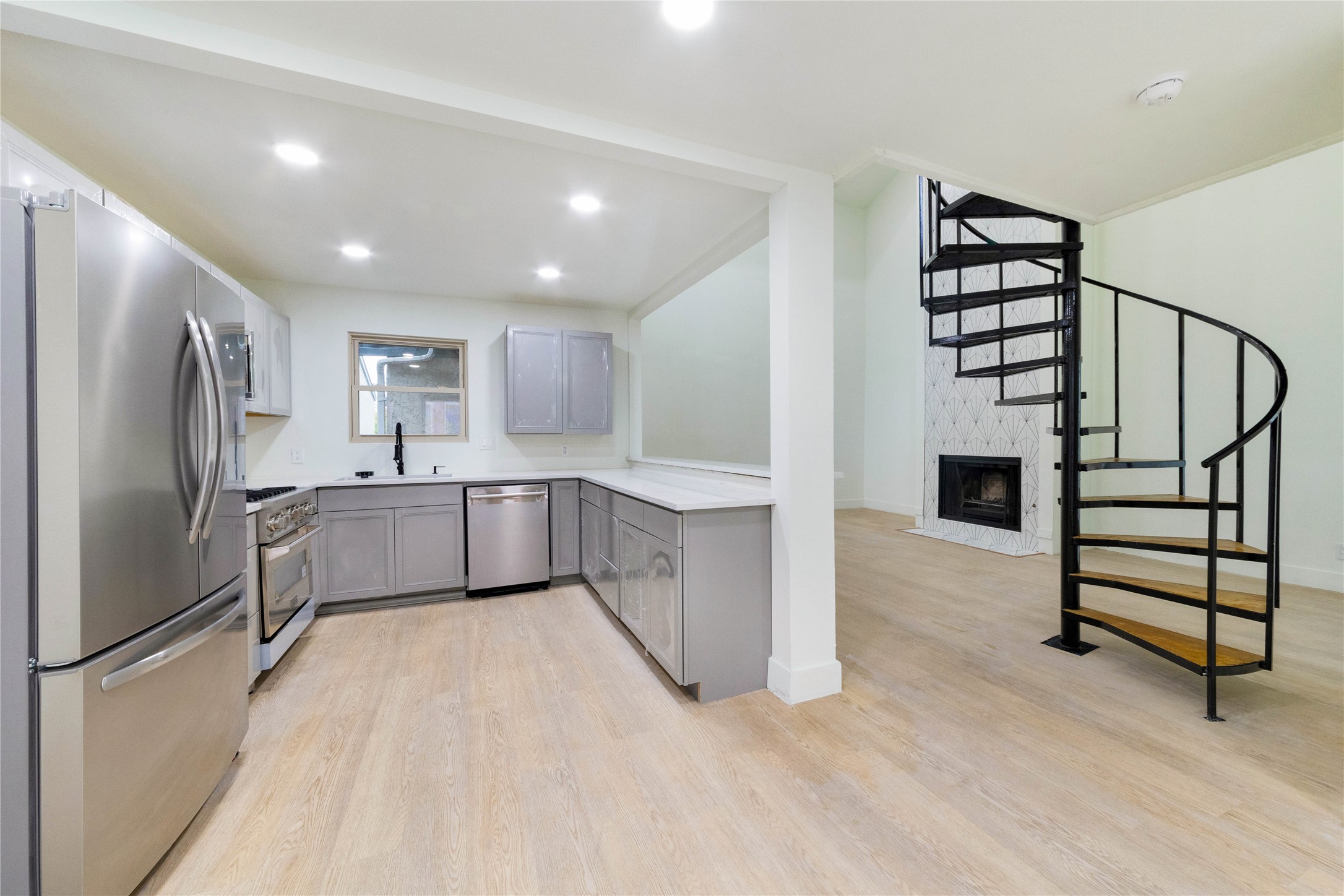 8807 Merion Circle Austin, TX 78754 - Photo 4 of 18 Modern kitchen with stainless steel appliances connects to a cozy living space featuring a spiral staircase and fireplace.