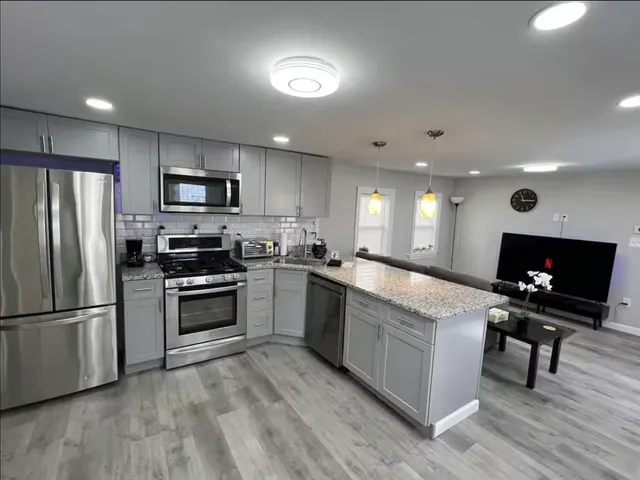 a large kitchen with stainless steel appliances kitchen island granite countertop a stove a sink dishwasher a refrigerator and a microwave with wooden floor