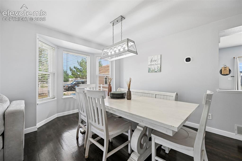 8347 Tibbs Road Peyton, CO 80831 - Photo 27 of 39 Dining area featuring a bay window, dark wood-finish flooring, and a white linear chandelier