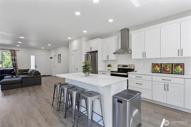 a kitchen with stainless steel appliances kitchen island granite countertop a stove a sink a refrigerator white cabinets and couches with wooden floor