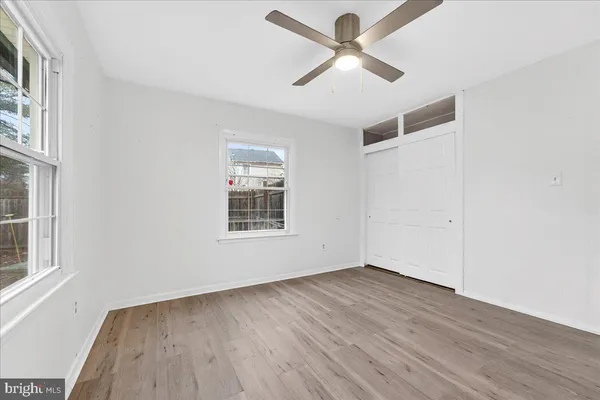 an empty room with wooden floor ceiling fan and windows