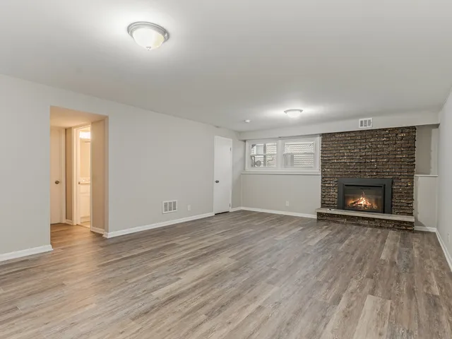 a view of an empty room with wooden floor fireplace and a window