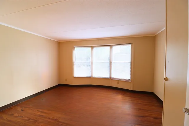 an empty room with wooden floor and windows with curtains