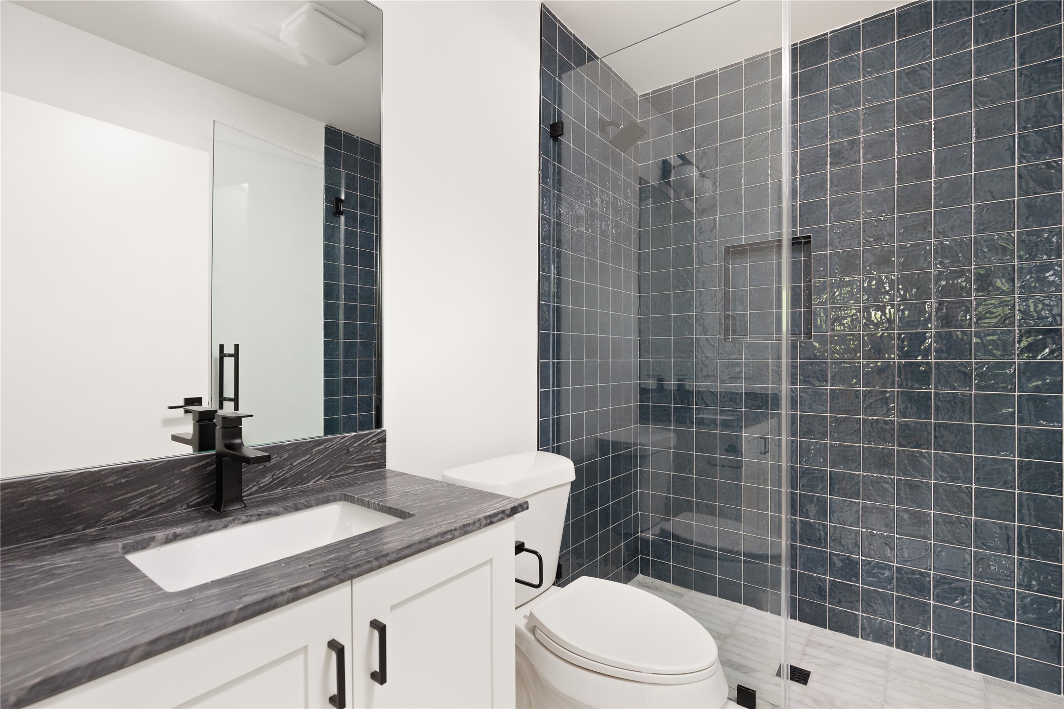 4501 Pack Saddle Pass Austin, TX 78745 - Photo 28 of 37 Full bathroom featuring a glass-enclosed shower with blue-toned square tile, a built-in shower niche, and a white vanity with a dark stone countertop and integrated sink