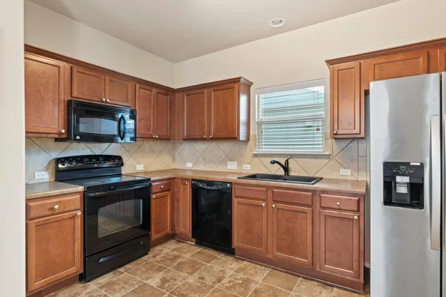 a kitchen with stainless steel appliances granite countertop a stove top oven a sink dishwasher and a refrigerator with wooden cabinets