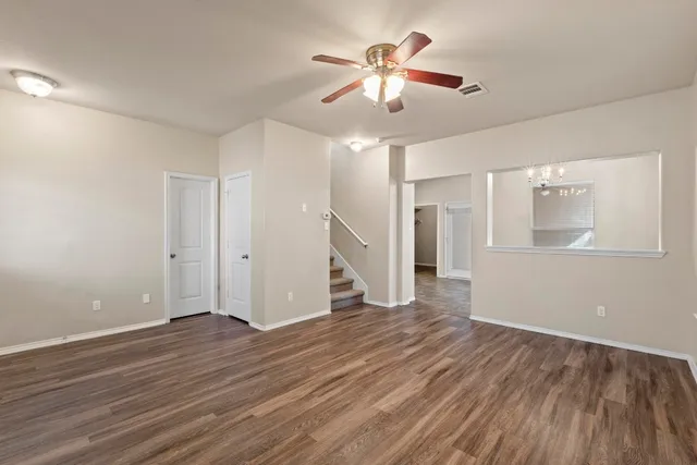a view of an empty room with wooden floor and a ceiling fan