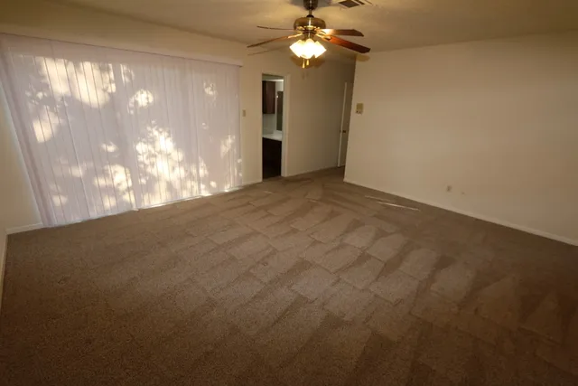 an empty room with a chandelier fan and windows