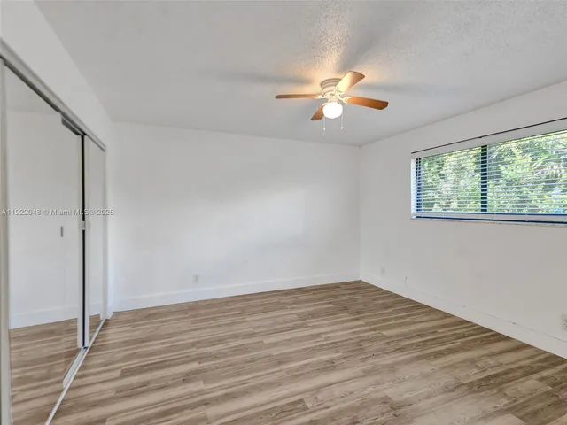 an empty room with wooden floor fan and windows