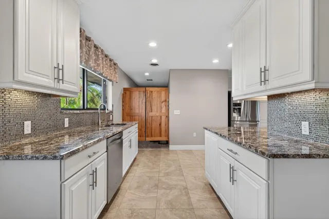 a kitchen with granite countertop a sink stainless steel appliances white cabinets and a window