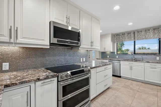a kitchen with granite countertop white cabinets white stainless steel appliances and a sink