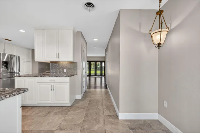 a kitchen with stainless steel appliances granite countertop a refrigerator a sink dishwasher a stove and white cabinets with wooden floor