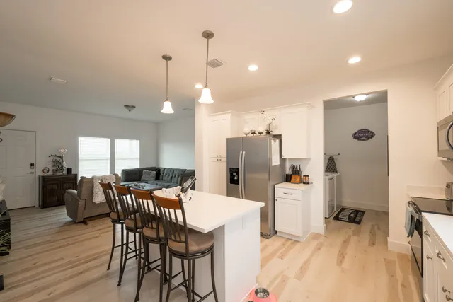 a kitchen with stainless steel appliances kitchen island granite countertop a dining table chairs and a refrigerator