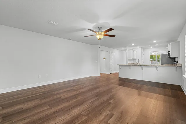a view of an empty room with kitchen and window