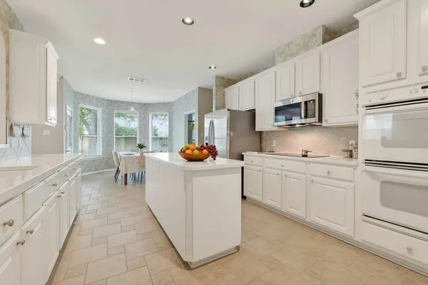 a kitchen with kitchen island granite countertop lots of white stainless steel appliances cabinets and a sink
