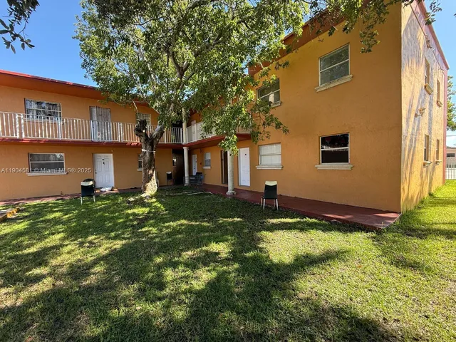 a backyard of a house with plants and large tree