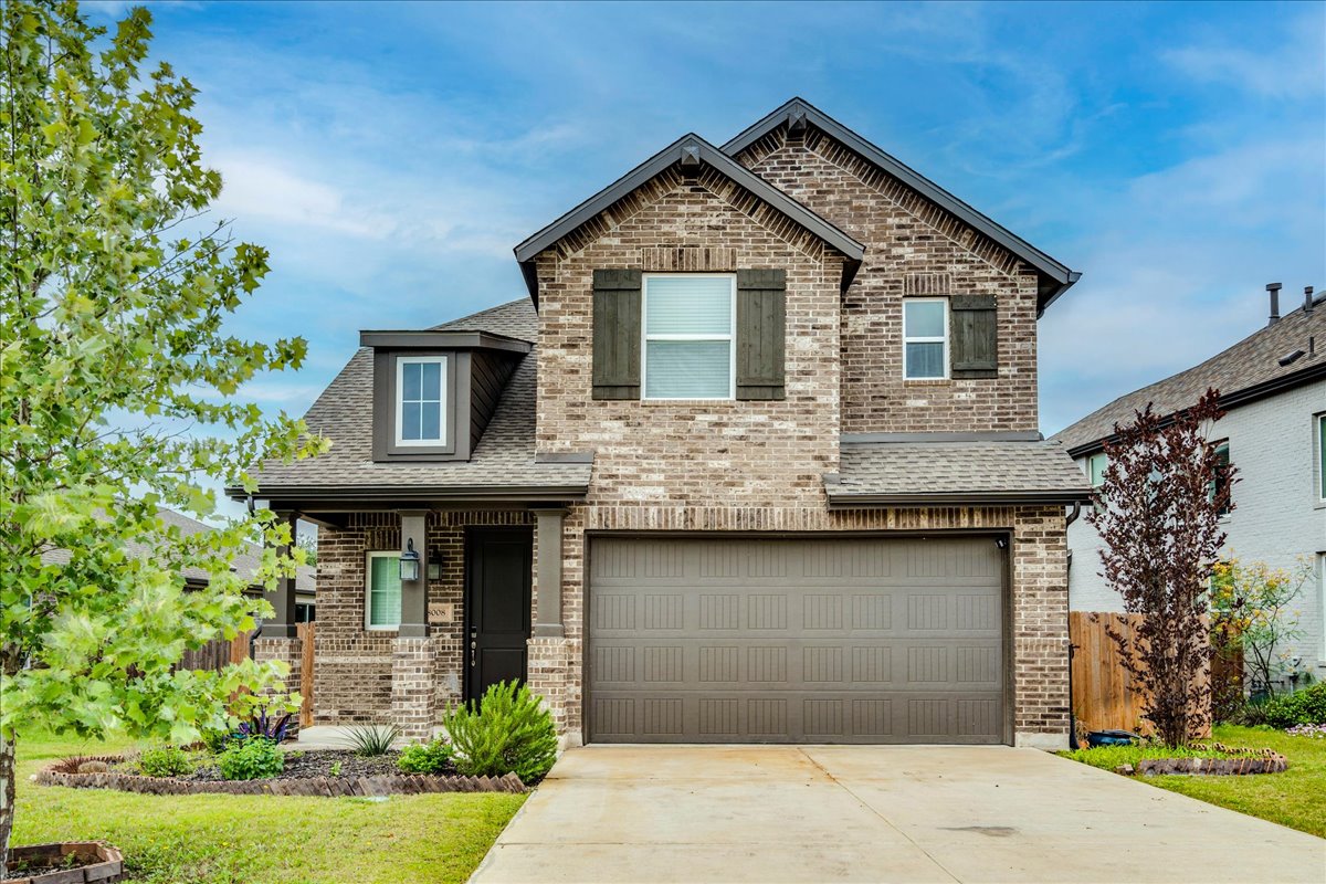 8008 Prairie Rye Drive Lago Vista, TX 78645 - Photo 1 of 40 Brick facade residence featuring a two-car garage, mature landscaping, and an inviting covered porch entrance