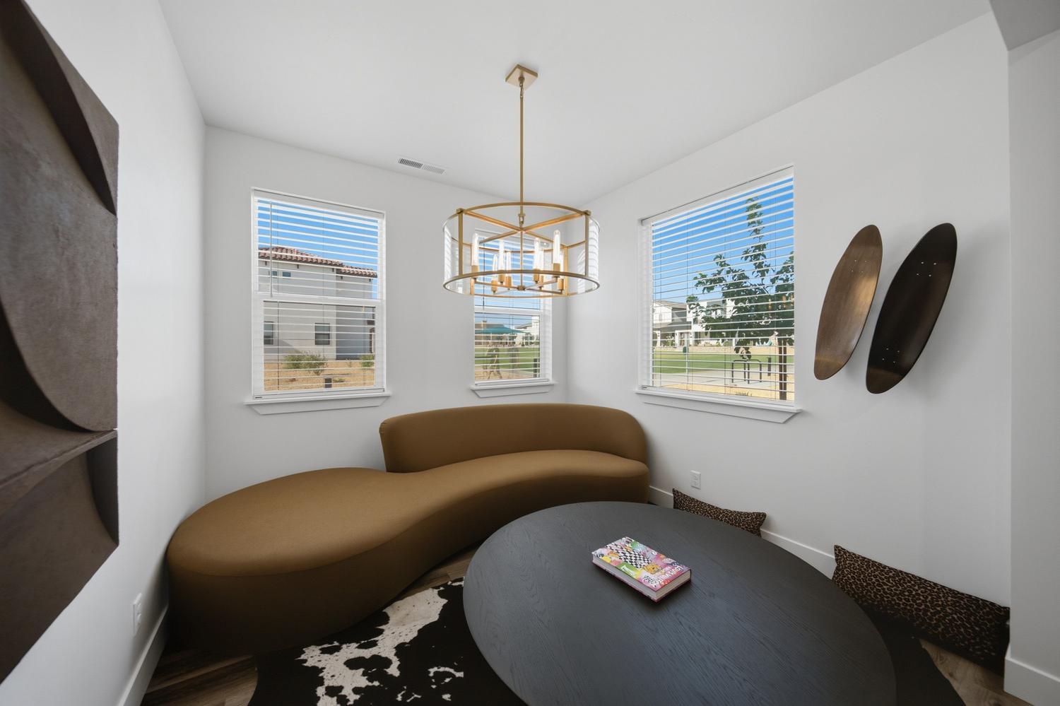 6144 Red Sand Lane St. George, UT 84790 - Photo 18 of 19 Bathed in natural light from three sides, this cozy den doubles as an art gallery, with bold abstract pieces flanking a curved caramel-hued chaise. The mixed-metal chandelier and cowhide rug lend a boutique-hotel feel to one of the home's most unexpected and stylish corners.