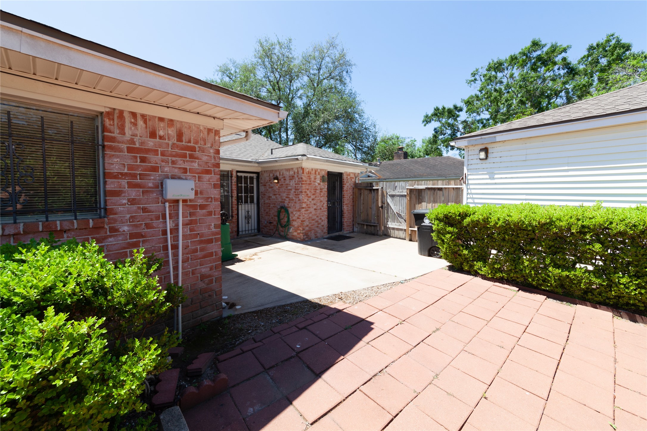 8826 Roos Road Houston, TX 77036 - Photo 40 of 42 A charming backyard with a mix of brick and siding exterior, featuring a spacious paved patio area, lush greenery, and a wooden privacy fence, ideal for outdoor activities and relaxation.