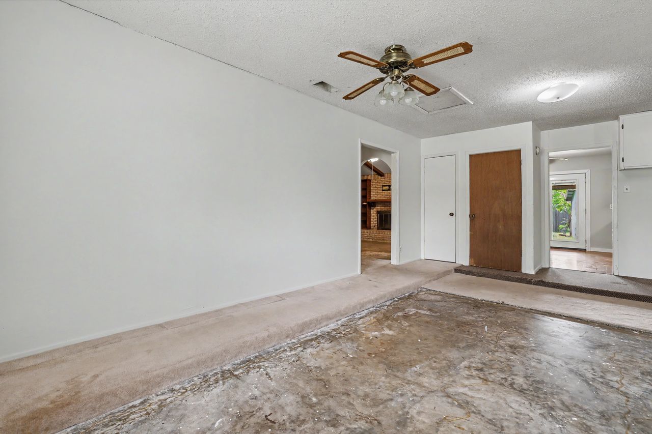 1811 Terry Lane Georgetown, TX 78628 - Photo 31 of 40 A versatile living space awaiting transformation, featuring a ceiling fan and a glimpse into an adjoining room with a brick fireplace.