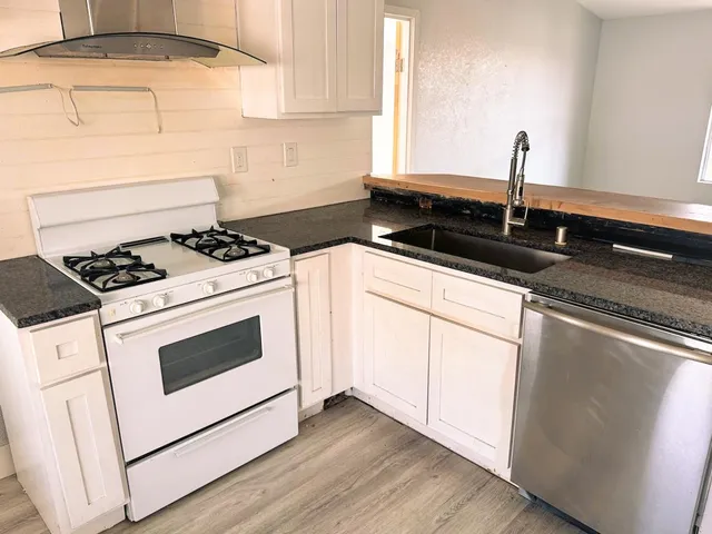 a kitchen with granite countertop stainless steel appliances a sink a stove and white cabinets