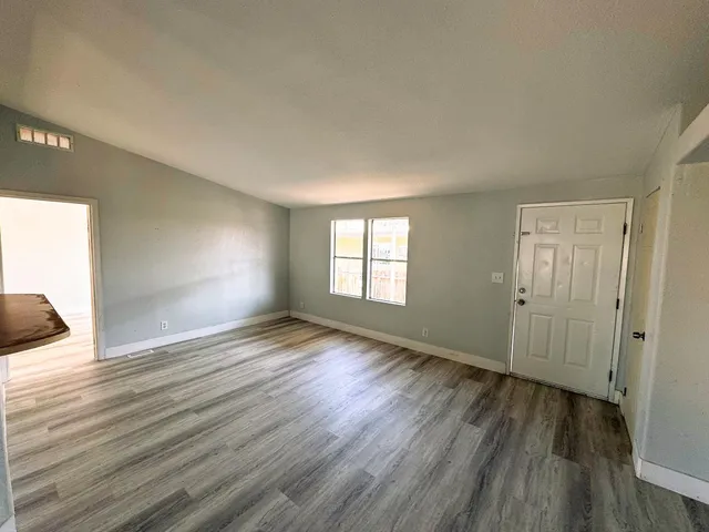 a view of an empty room with wooden floor and a window