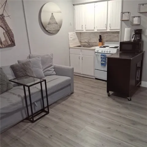 a living room with stainless steel appliances granite countertop a sink wooden floor and a window