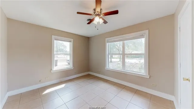 an empty room with chandelier fan and windows