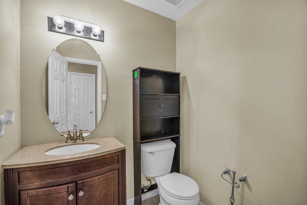 5718 Green Ivy Road Denton, TX 76210 - Photo 15 of 37 Powder room featuring a curved wood-finish vanity with a light-toned countertop, oval mirror, and three-bulb vanity light fixture