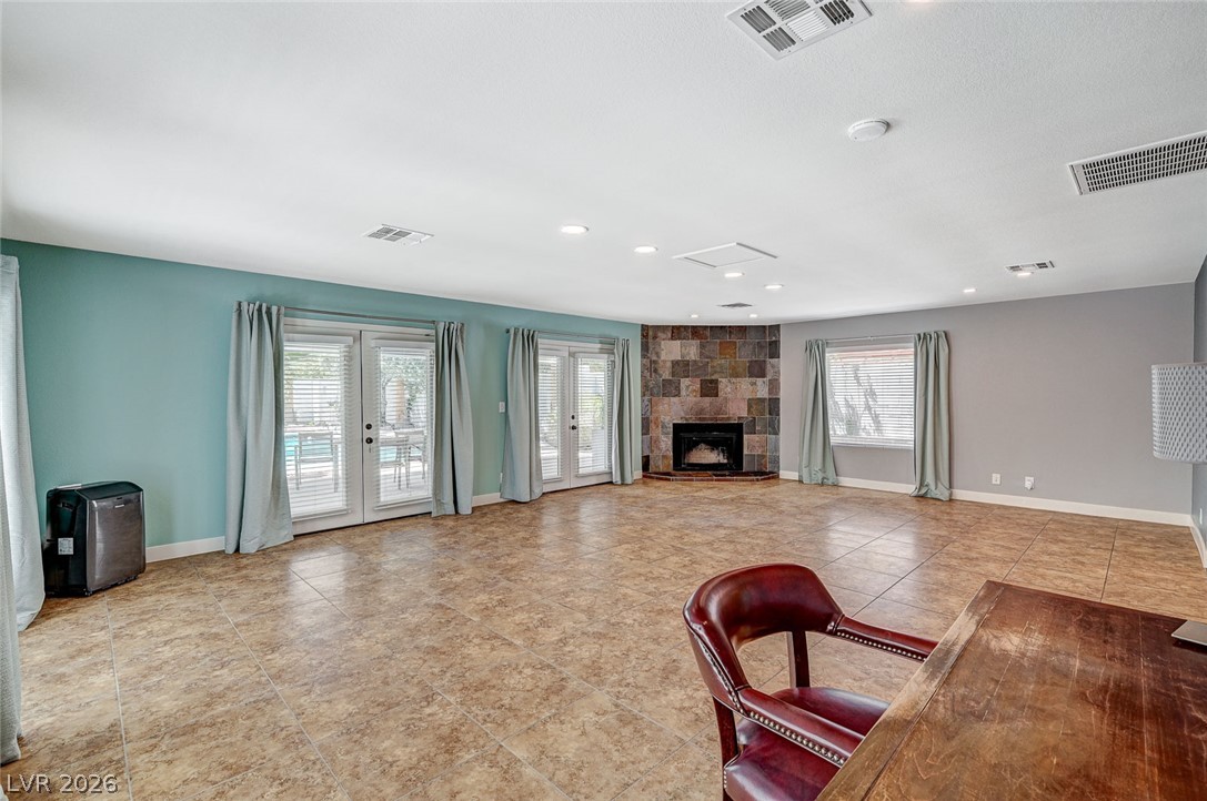 4153 Woodcrest Road Las Vegas, NV 89121 - Photo 25 of 58 A spacious living area featuring tiled floors, a stone-clad corner fireplace, and multiple French doors opening to outdoor leisure.