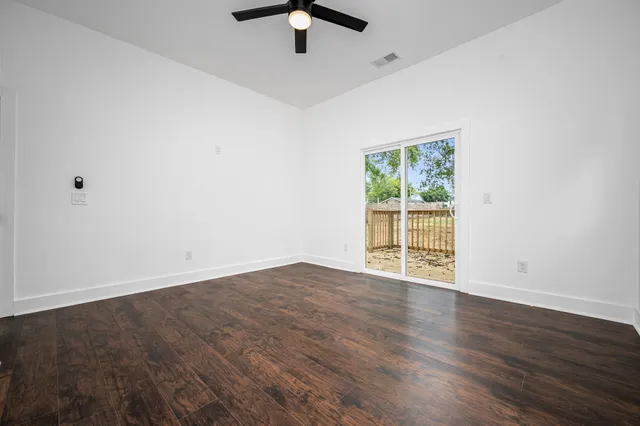 an empty room with wooden floor fan and windows