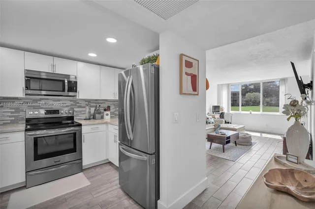 a kitchen with stainless steel appliances a refrigerator a stove a microwave a sink dishwasher and white cabinets with wooden floor